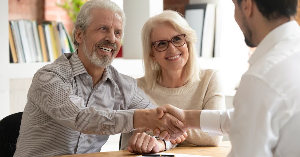 A middle-aged couple in a meeting with a professional man shaking hands